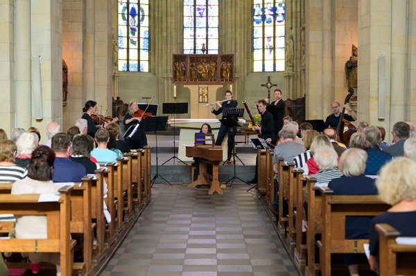 Musiker mit Instrumenten in einer kleinen Kirche, vollbesetzte Bänke